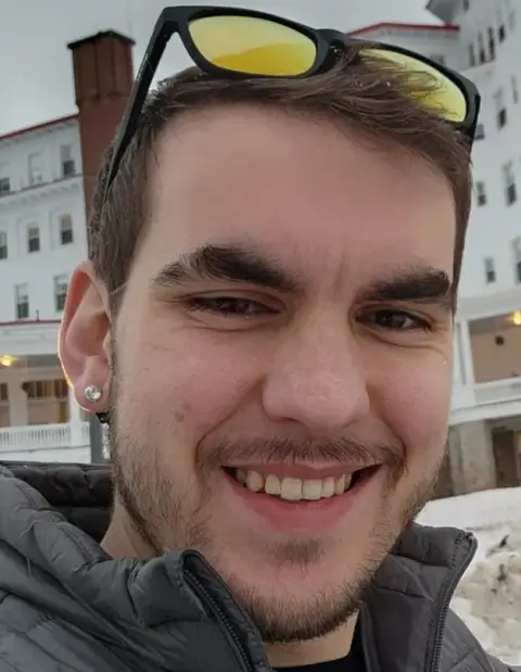 David Huson smiling in a gray jacket with a white building in the background.